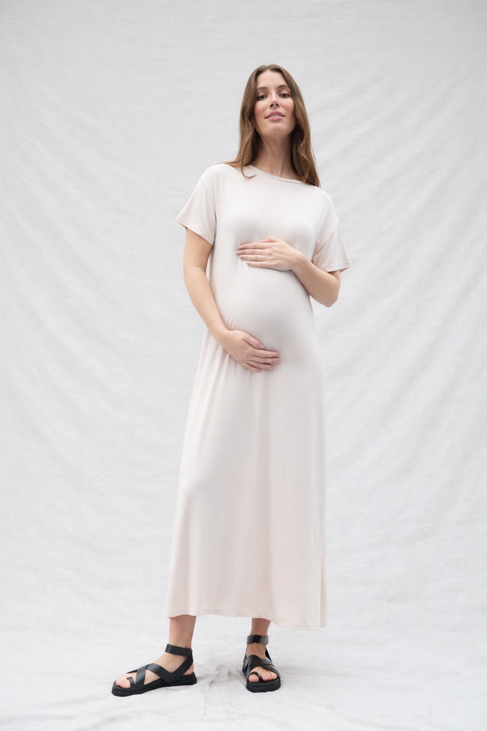 Pregnant woman wearing an oat-colored dress against a white background