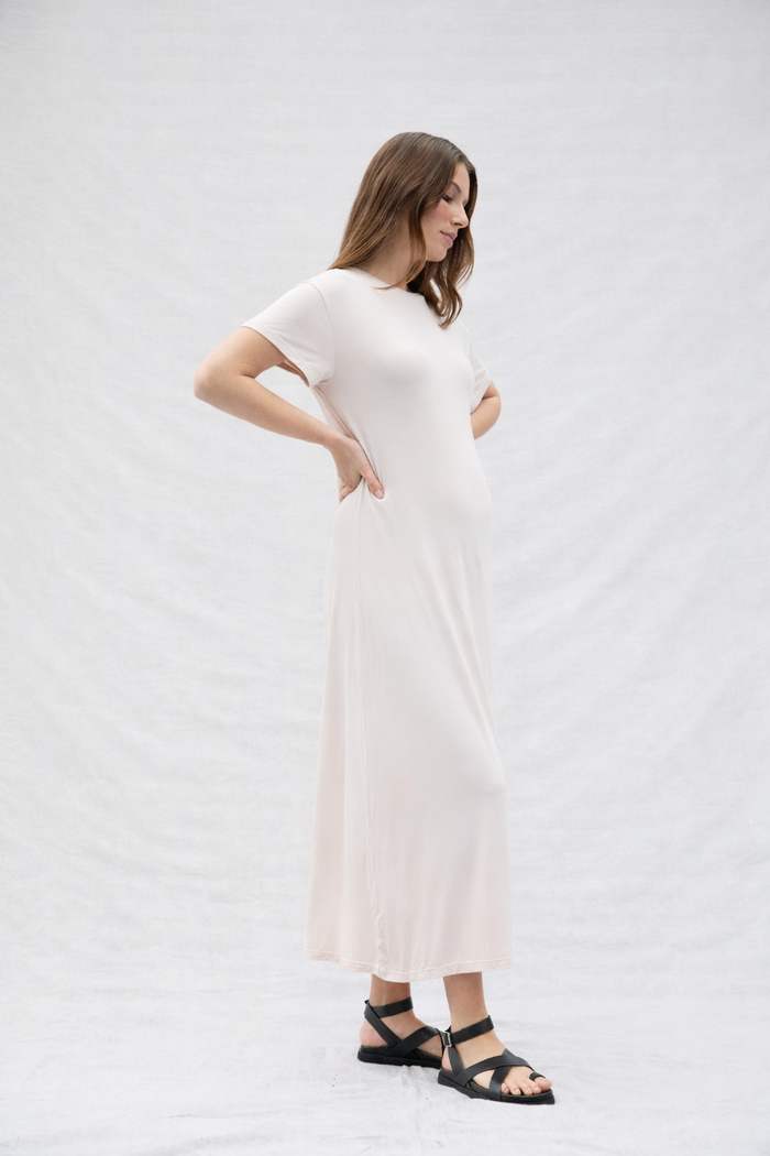 Pregnant woman wearing a oat coloured dress on a plain background