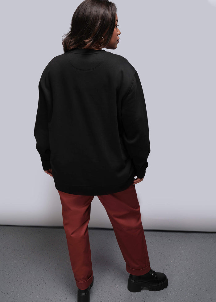 1X=Person wearing a black sweatshirt and red pants standing against a plain background