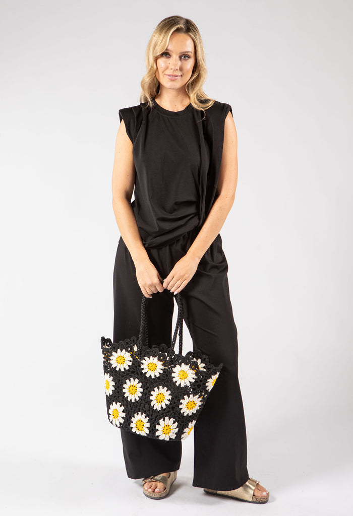 Woman holding a black tote bag with white daisy patterns against a white background