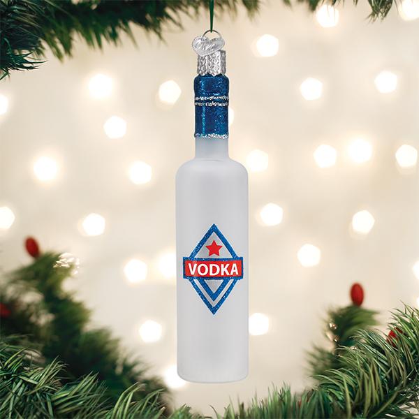 A Christmas tree ornament shaped like a frosted vodka bottle hangs among green pine branches, with blurred white lights in the background. The bottle has a blue label with a red star and the word VODKA.