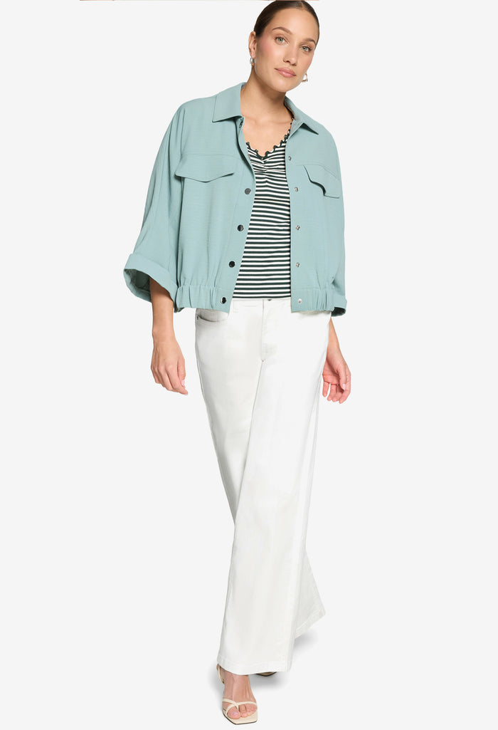 Woman wearing a light blue denim jacket, striped shirt, and white pants on a white background